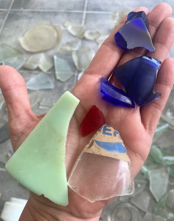 A hand holding a handful of sea glass finds in cobalt blue, seafoam green, red and frosted white.